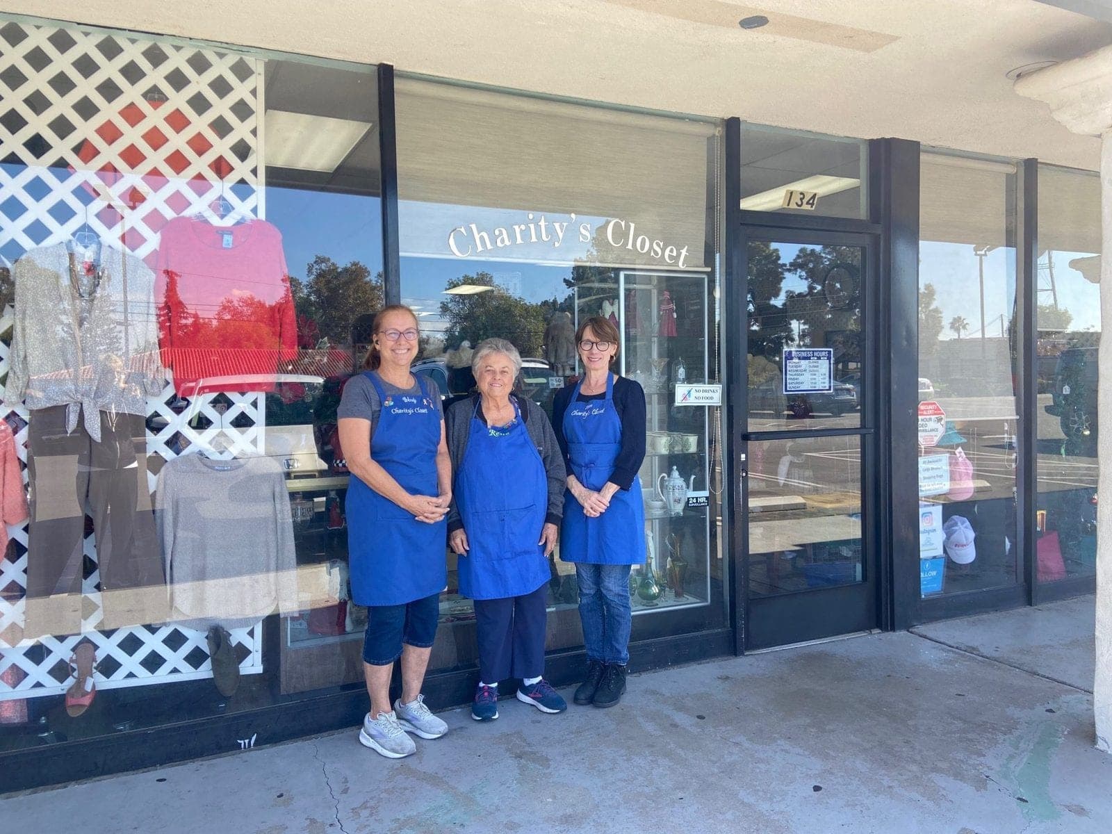 Three volunteers in blue aprons in front of the Charity’s Closet shop window